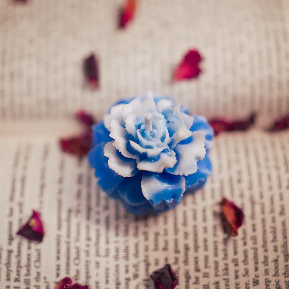 Blue and white peony rose flower-shaped candle on a book with petals around