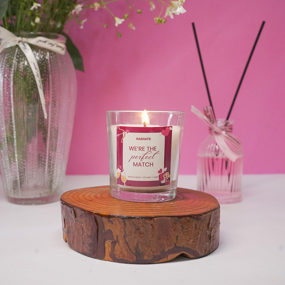 We're a perfect match cherry blossom scented candle by radiate on a wooden coaster against pink background.
