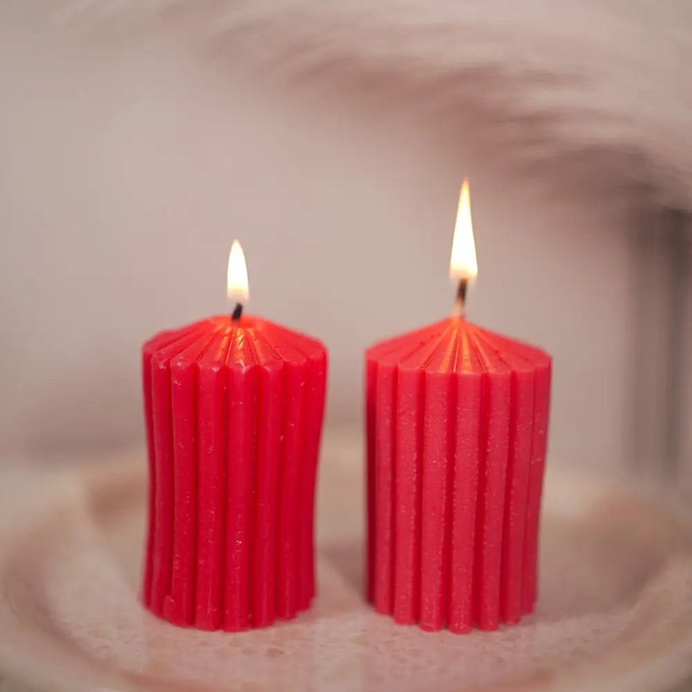 Two red stripped lines ribbed pillar candles by Radiate with wicks lit on a textured surface