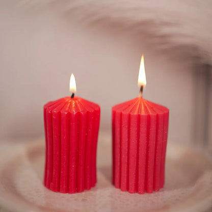 Two red stripped lines ribbed pillar candles by Radiate with wicks lit on a textured surface