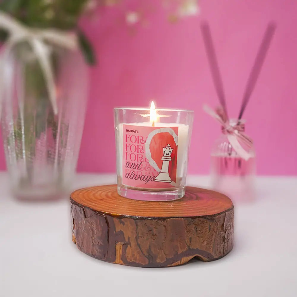 Radiate's queen scented candle with floral scent on a wooden coaster against a pink background. 