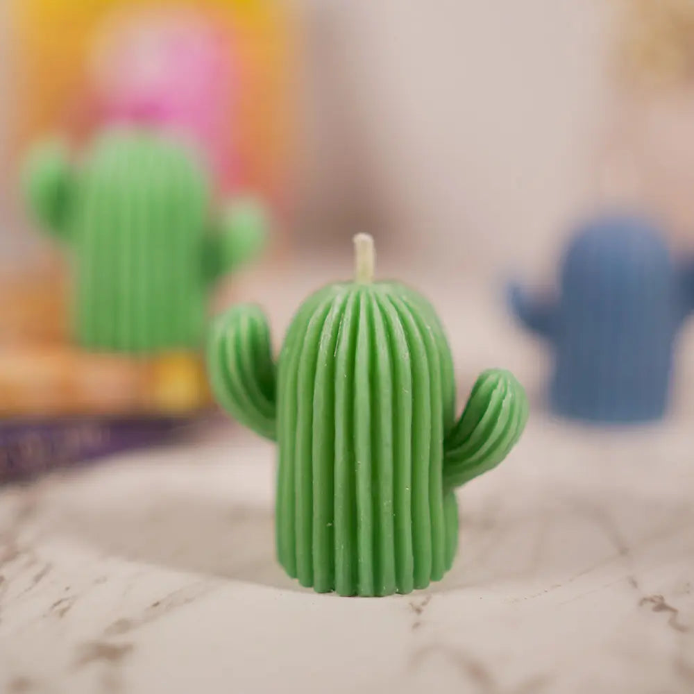 Cactus-shaped candle on a textured surface with a blurred colorful cactus candles in background