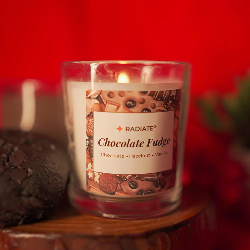 Chocolate fudge scented candle on wooden coaster by Radiate with a Fudge cake on side set against a red background 