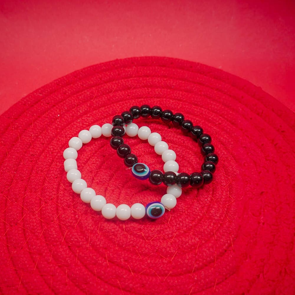 Two matching evil eye bracelet in white and black color on a red surface