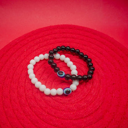 Two matching evil eye bracelet in white and black color on a red surface