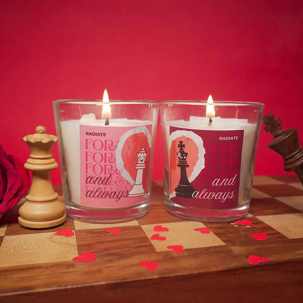 Two lit candles for king and queen  with chess pieces and hearts on a checkered surface against a red background.