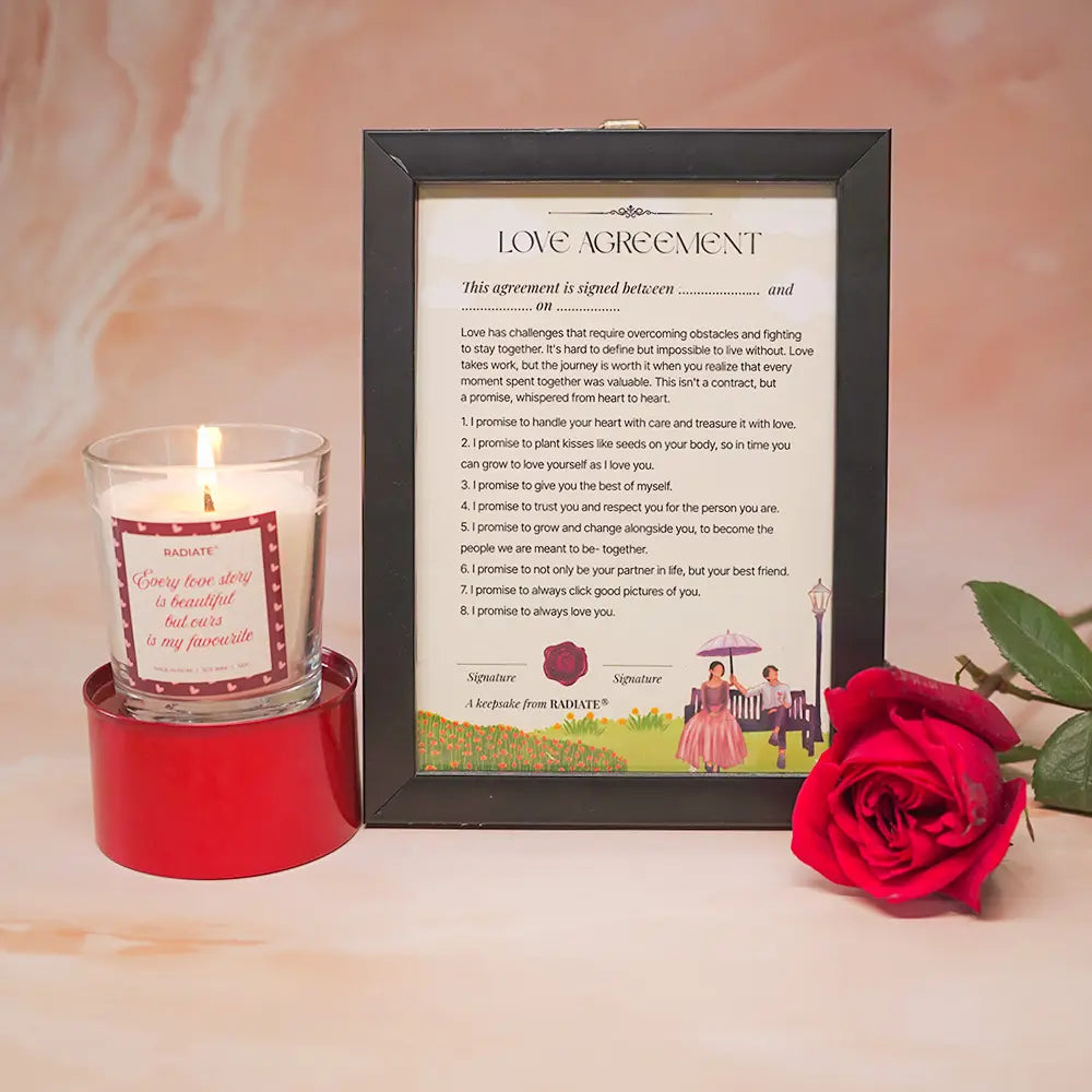 Framed 'Love Agreement' document with a lit love story scented candle and red rose on a soft pink background