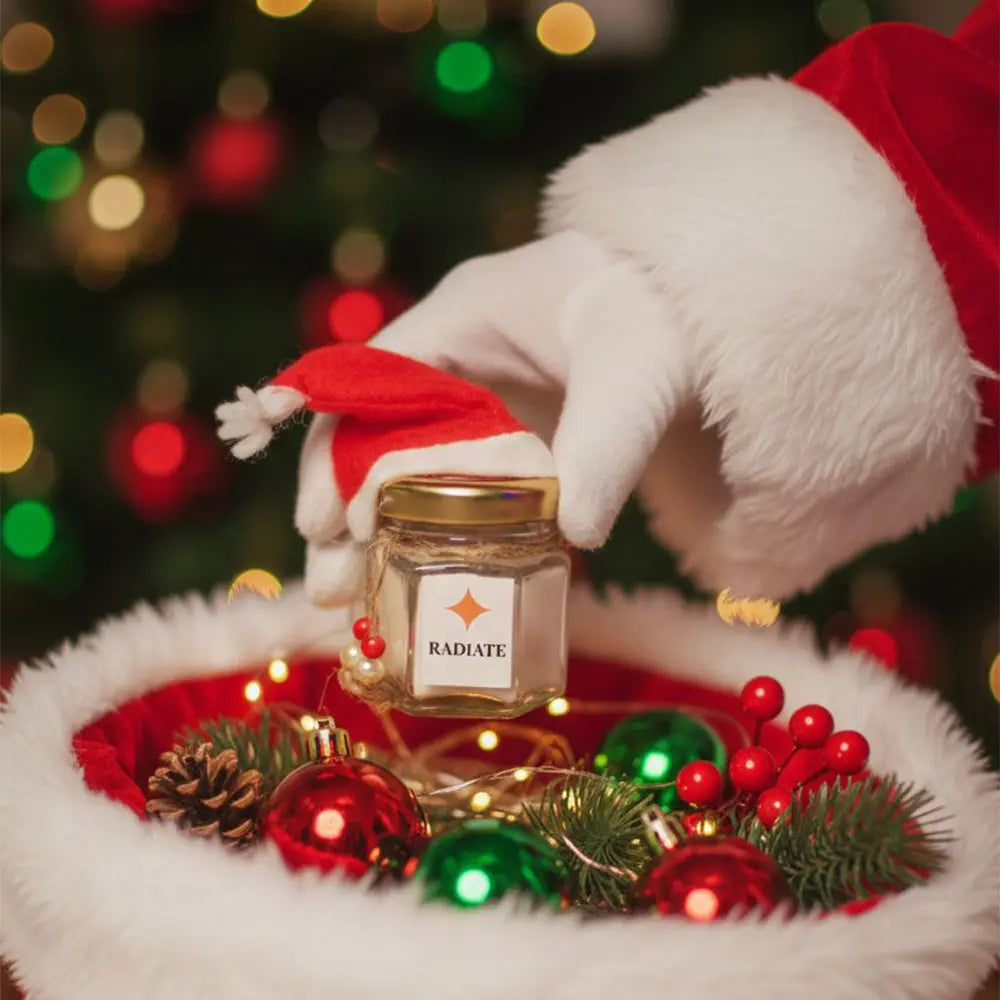 Santa hand holding a chocolate fudge scented candle by 'Radiate' with Christmas decorations in the background.