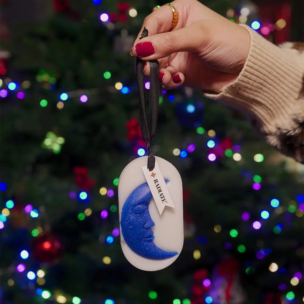 Hand holding a wax sachet with a moon face design by Radiate against a festive background with colorful lights.