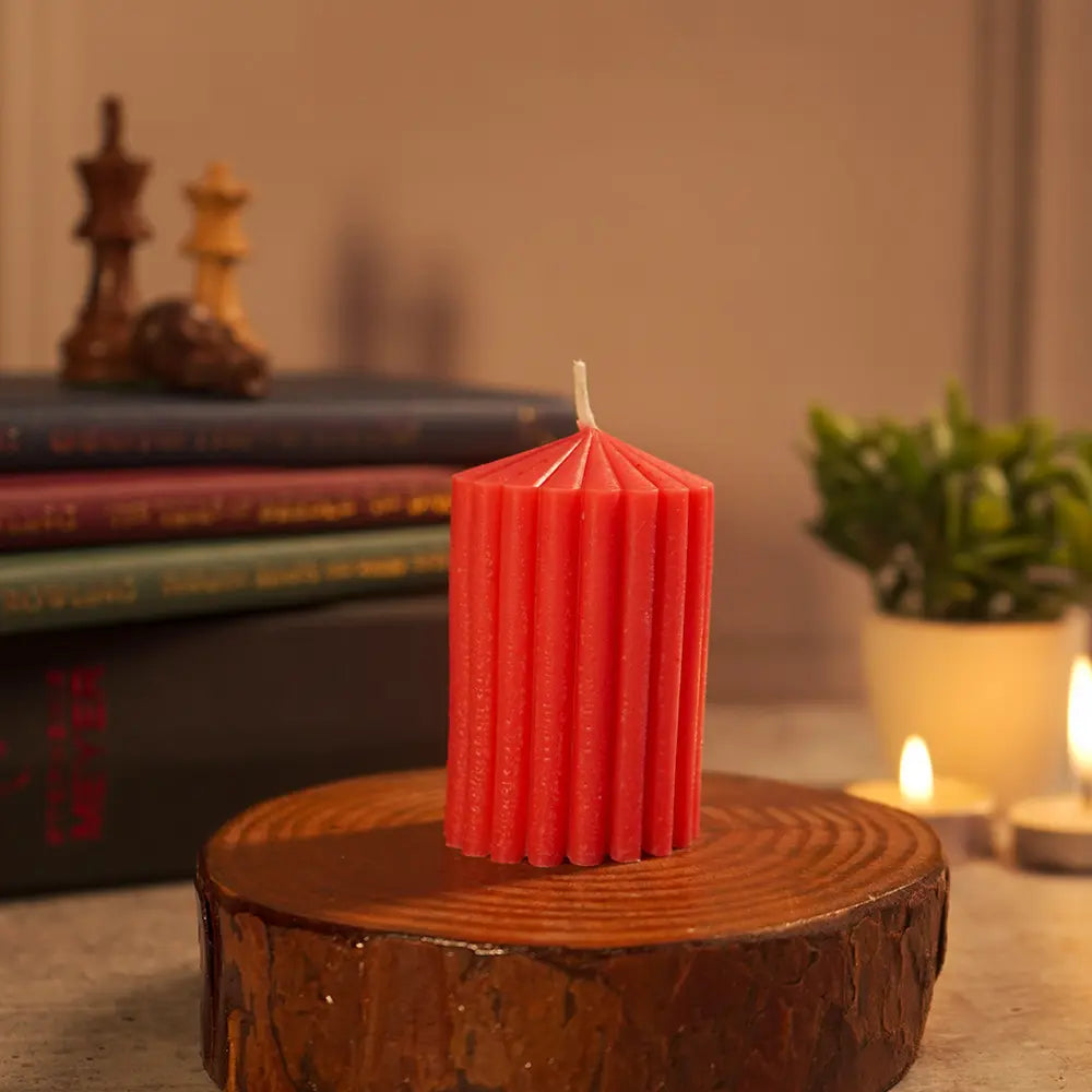 Red stripes ribbed scented pillar candle by Radiate on a wooden stump with books and plants in the background. Table, home decor. 