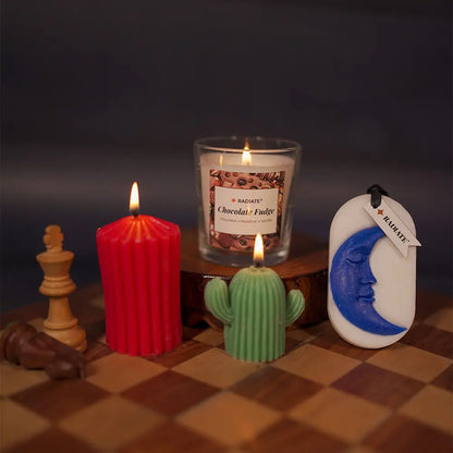 Weekend reset gift box by Radiate featuring s a Chocolate fudge scented candle, cactus-shaped pillar candle, red stripped pillar candle, and moon fragrance tablet on a chess board with a dark background