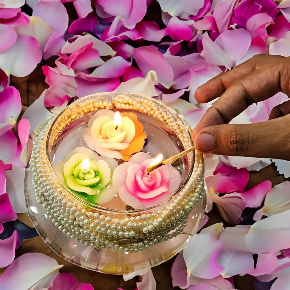 Hand lighting rose flower floating candle in a bowl on a bed of pink rose flowers.