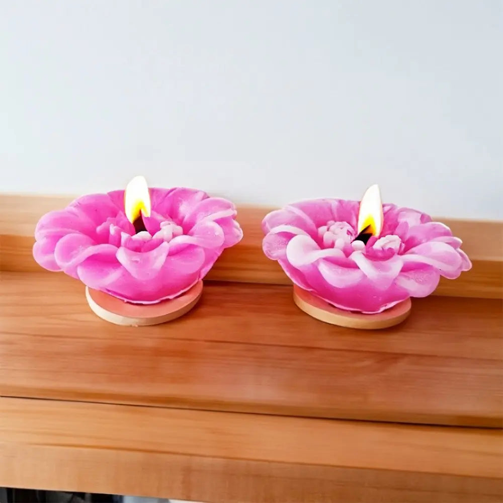 Two pink flower-shaped floating candles with flames on a wooden surface.