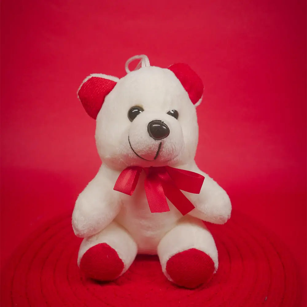 White teddy bear with a red bow on a red background