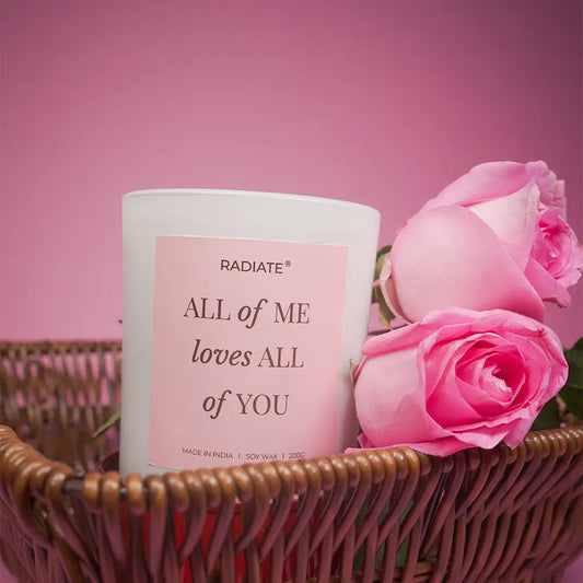 All of me scented candle in a basket surrounded by rose flowers on a pink background. 