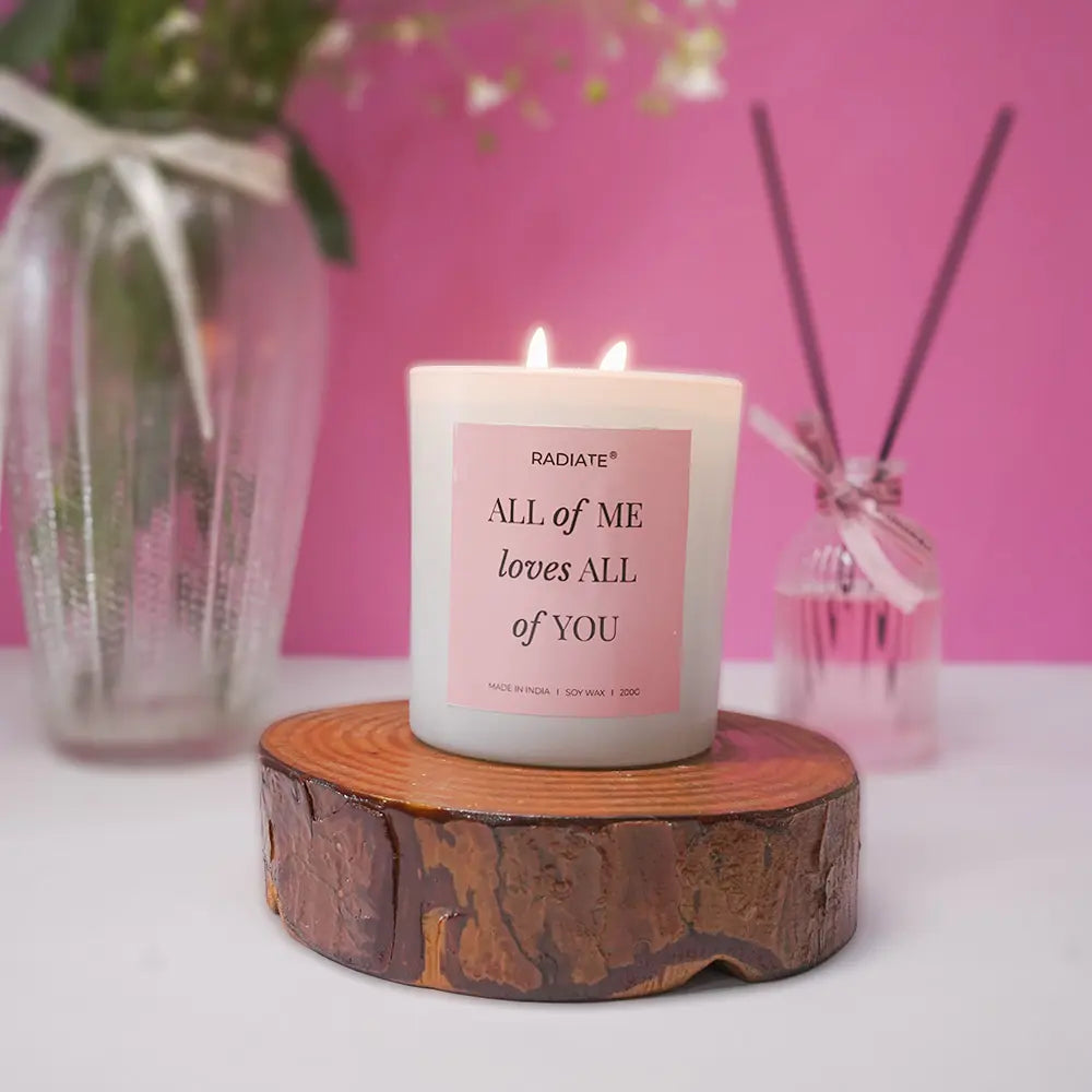All of me musk scented candle with a romantic message on a wooden stand against a pink background
