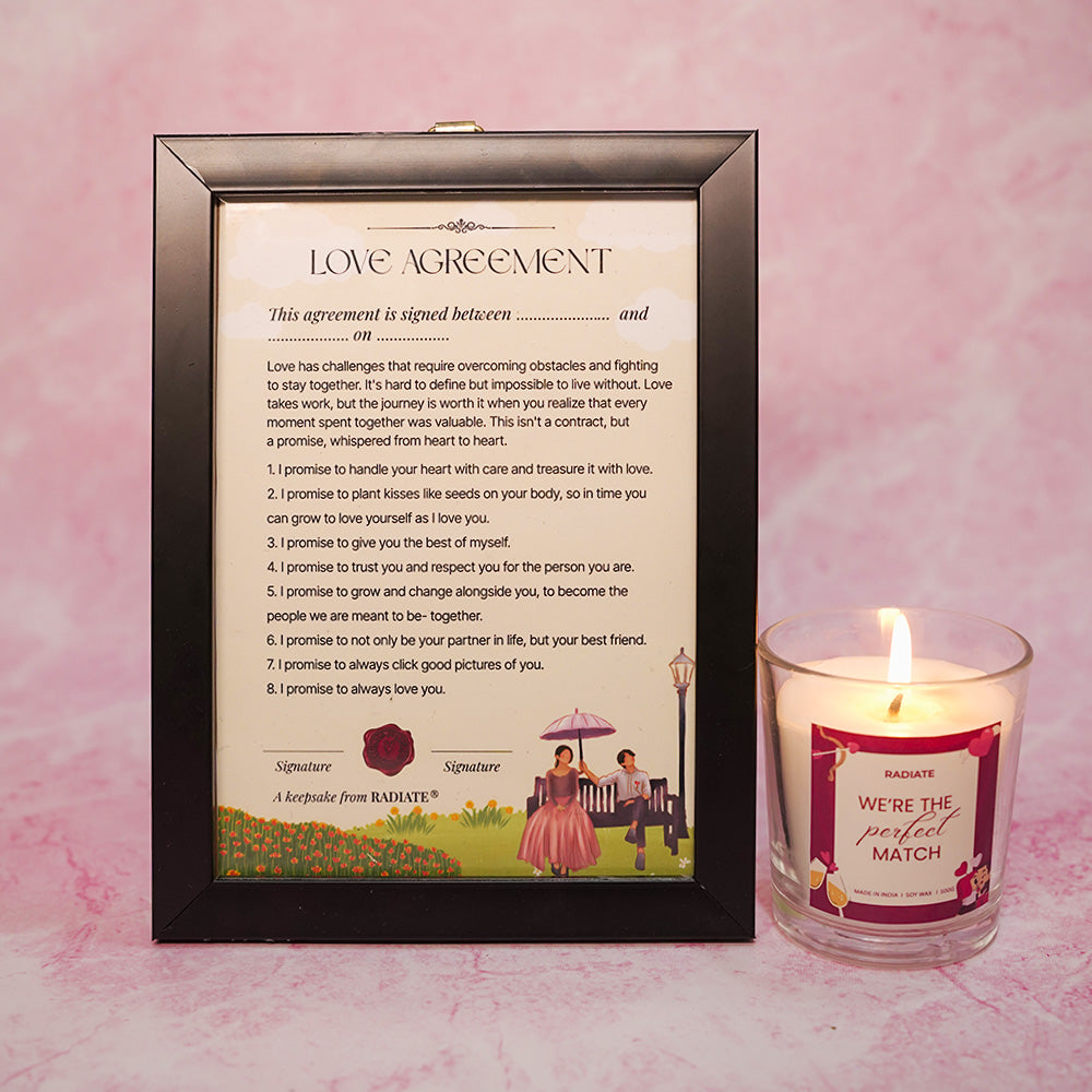 Framed 'Love Agreement' document with a lit 'perfect match' cherry blossom scented candle on a pink background