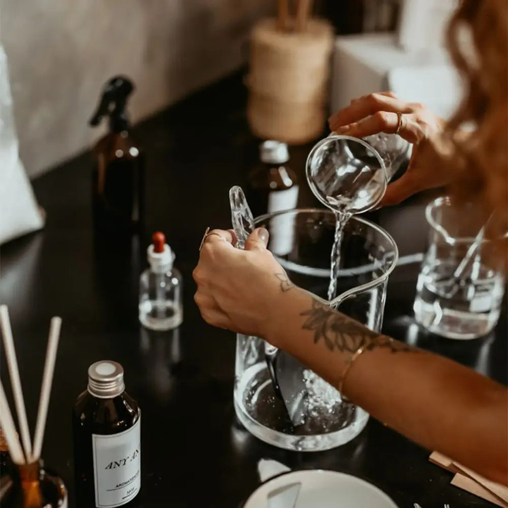 Person preparing a fragrance mix with essential oil bottles and other ingredients on a table.