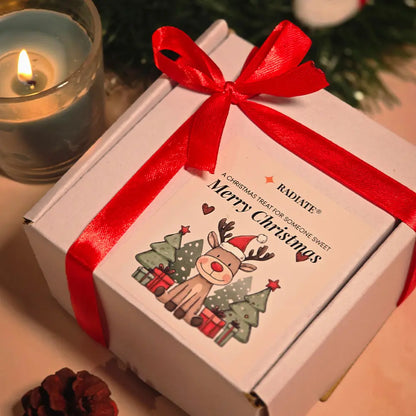 Radiate candle gift box with a red ribbon and Christmas-themed label, next to a lit candle and pine cone.