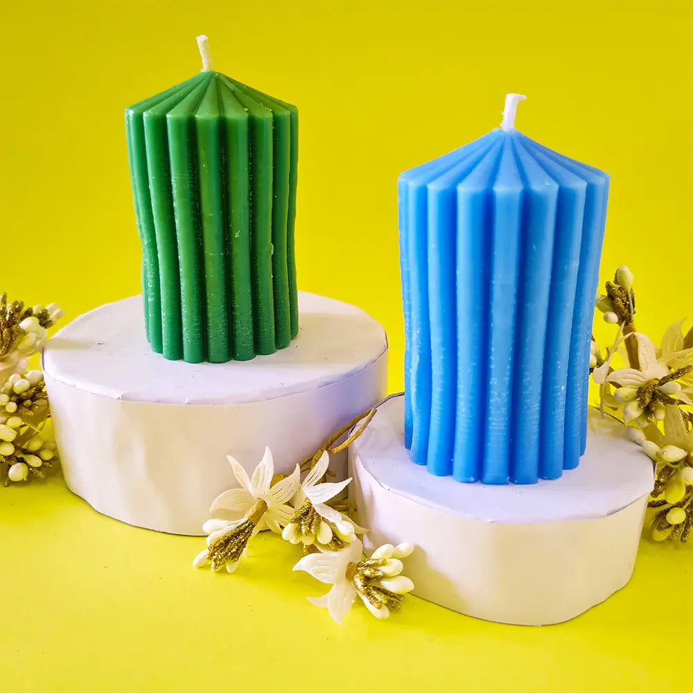 Two ribbed lines scented pillar candles, one green and one blue, on white stands with a yellow background.