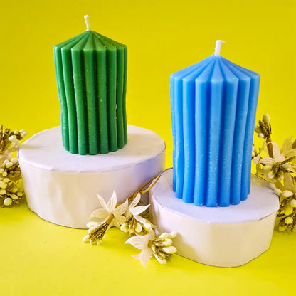 Two ribbed lines scented pillar candles, one green and one blue, on white stands with a yellow background.