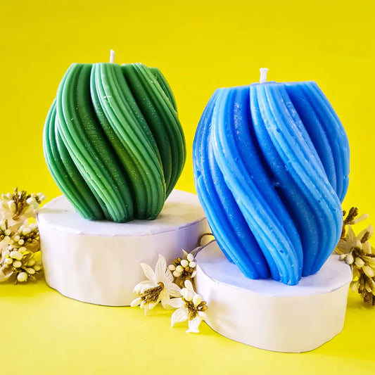 Two green and blue spiral swirl wave scented pillar candles on white podiums with a yellow background