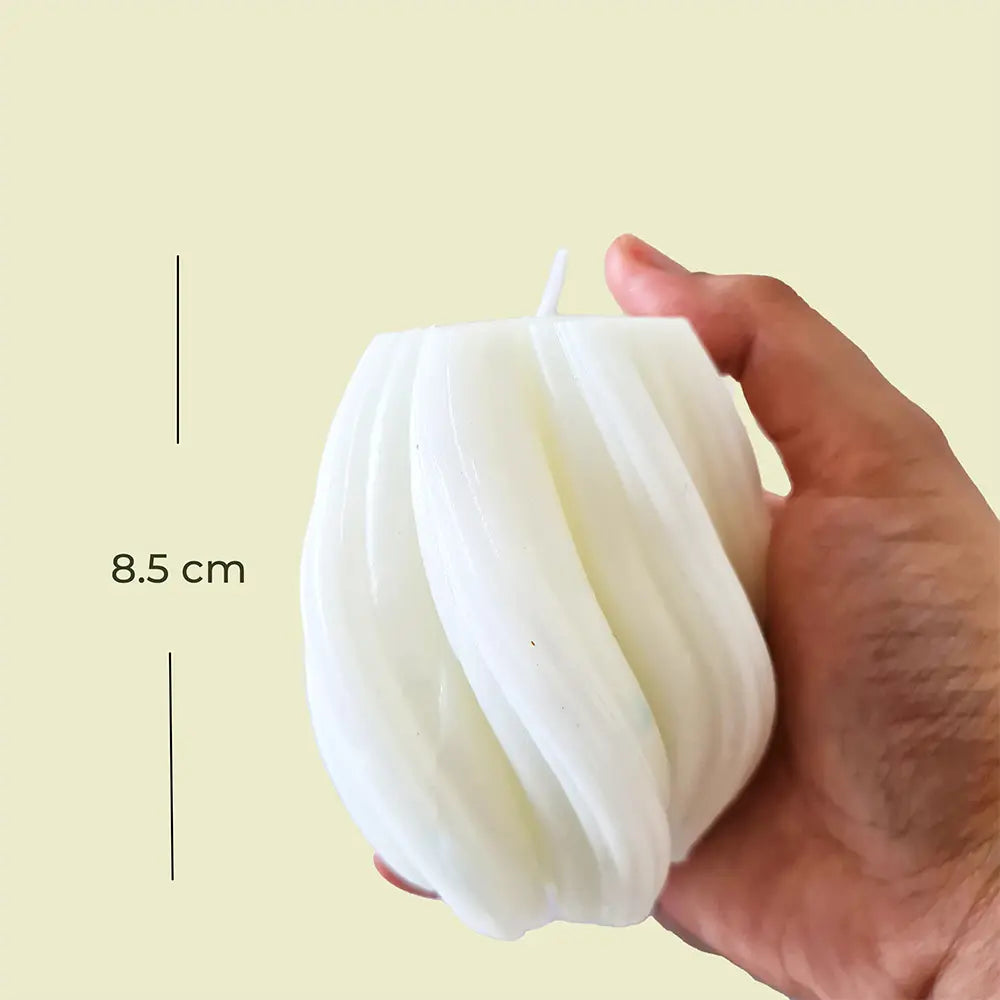Hand holding a white swirl shaped candle with it's measurement on a beige background.