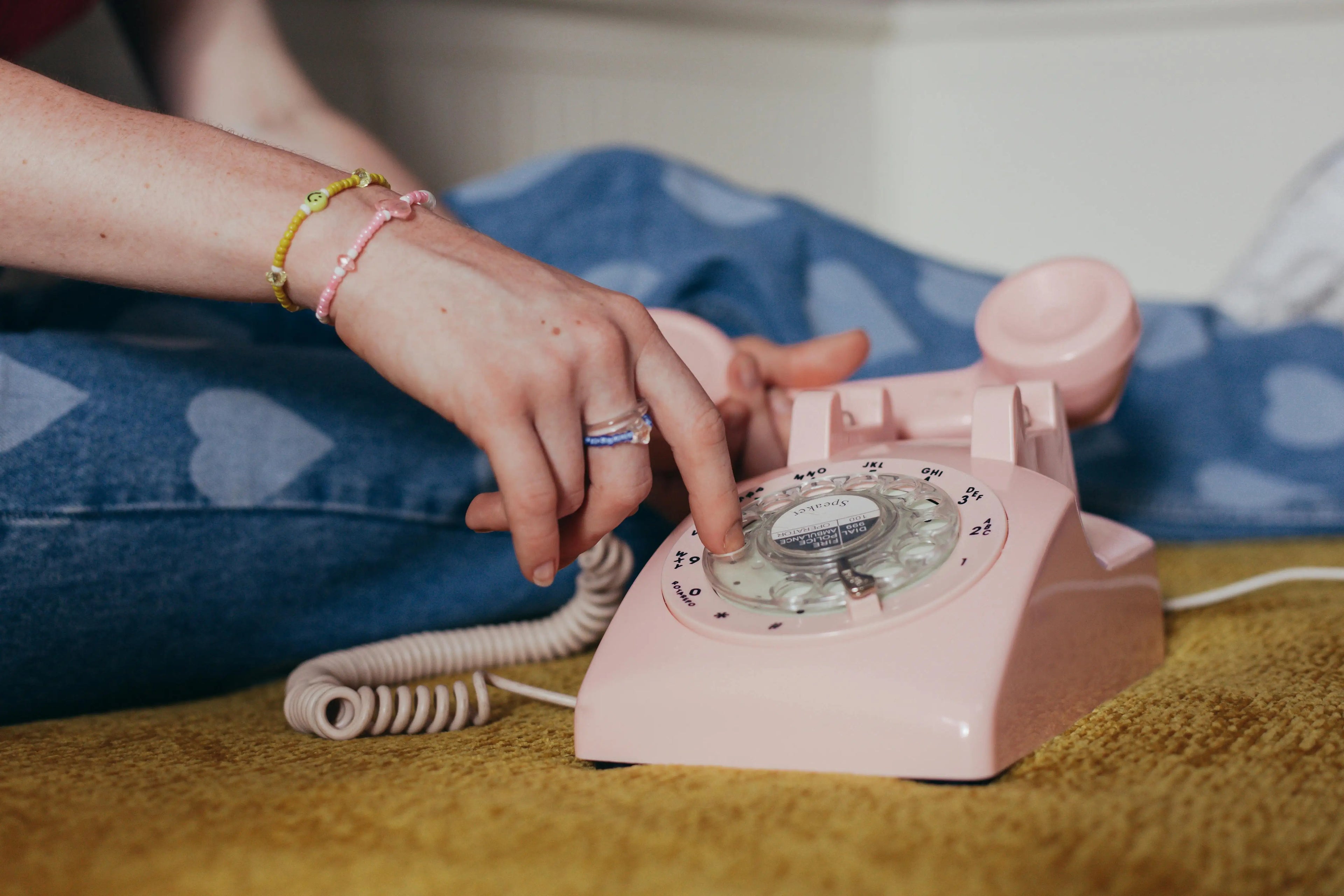 Person using a pink rotary phone on a yellow surface with blue fabric in the background
