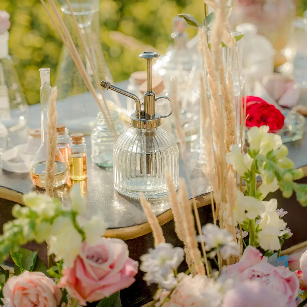 Decorative table setting with flowers, flasks, and a spray bottle on a blurred natural background