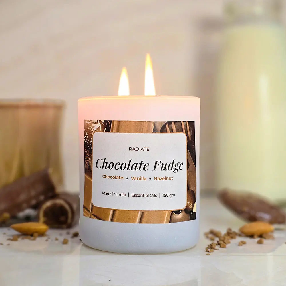 Radiate's Chocolate Fudge scented soy wax candle with aroma of Chocolate, Hazelnut and vanilla, surrounded by chocolate pieces, nuts, cup of hot chocolate and milk bottle on a light background.