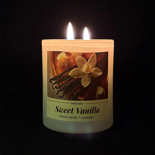 Radiate's Sweet vanilla scented soy wax candle light up with two flames with vanilla beans and flowers on a dark background